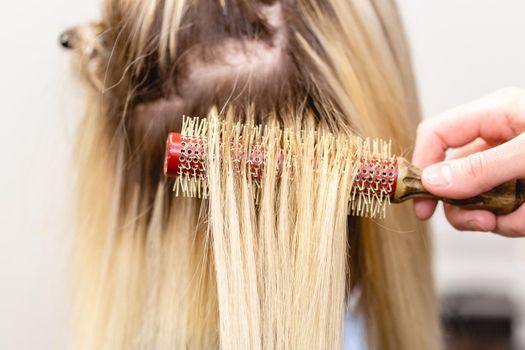 Hair extensions correction procedure. Hairdresser does hair extensions to blonde hair lady in a beauty salon
