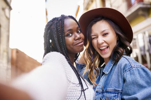 Two multiethnic women making selfie and grimacing with a smartphone.