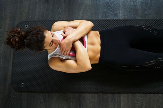 Sporty young female, wearing sportswear, on yoga mat doing situps with plate weights in gym. Fitness woman doing abs crunches.