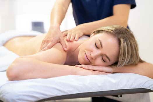 Young woman lying on a stretcher receiving a back massage in a spa center.