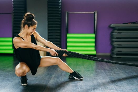 Young and athletic woman using training ropes in a gym. Fitness concept.