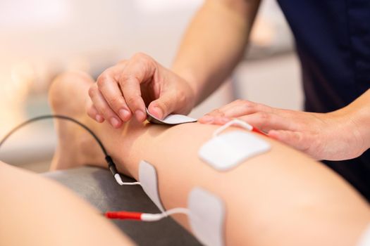 Physiotherapist applying electro stimulation in physical therapy to a young woman.