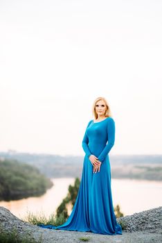 blonde girl in a blue dress with blue eyes in a granite quarry against the background of gravel