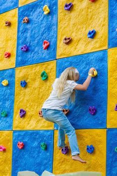 A little Girl Climbs a Stone Wall in a children's center.