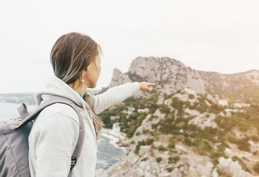 Backpacker young woman pointing at cliff on coastline. Image with sunlight effect.