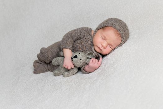 Lovely newborn boy with chubby cheeks in brown knitted clothes sleeps with a hare toy in his small hand.