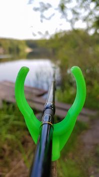 Fishing rod feeder on a stand against a lake. Close fishing on the river, fishing rod stands on a green slingshot.