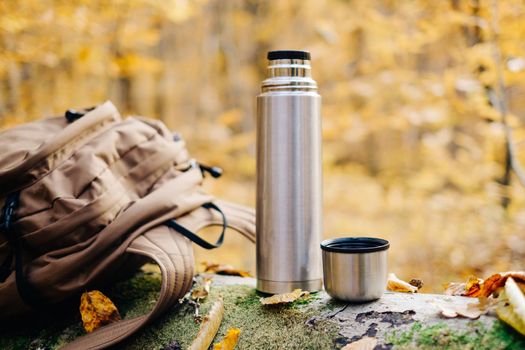 Backpack and thermos bottle on fallen tree trunk in autumn forest.