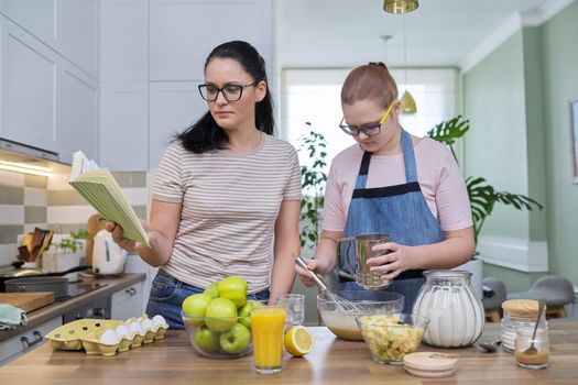 Mom and preteen daughter cooking together at home in kitchen apple pie, mother with book of recipes reading sequence of baking. Family, lifestyle, parent child relationship, homemade food concept