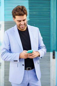 Young businessman wearing blue suit using a smartphone in urban background. Man with formal clothes in the street.