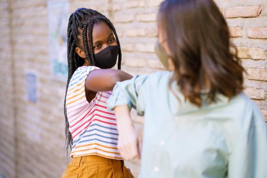 Multiethnic young women wearing masks greeting at each other with their elbows outdoors