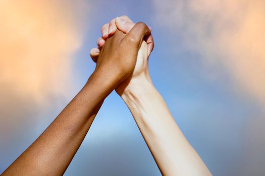 Close up of multiethnic women's hands together against cloudy sky.