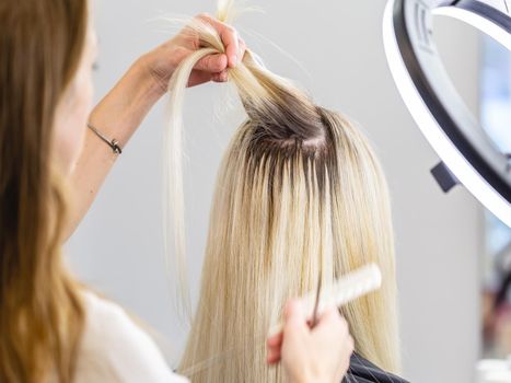 Hairdresser separates her clients blonde hair from hair extensions for correction procedure in beauty parlour