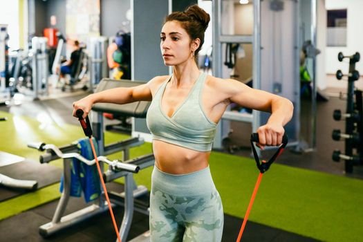 Young sportswoman warming up with fitness gums in the gym wearing sportswear