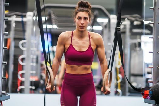 Athletic woman doing some pull up exercises in the gymnastic rings in a gym