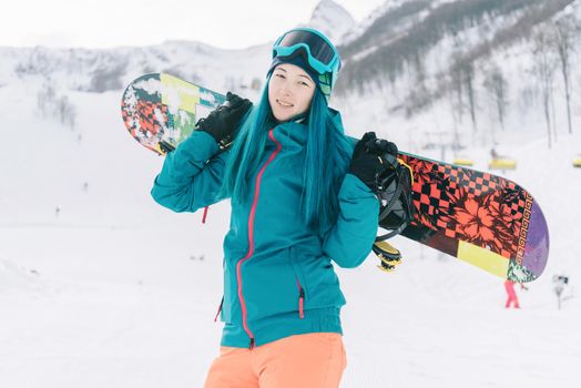 Sporty young woman standing with snowboard on ski resort in winter outdoor, looking at camera.