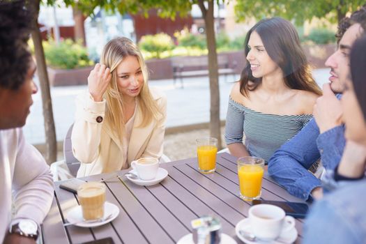 Multi-ethnic group of friends having a drink together in an outdoor bar. Young people having fun.