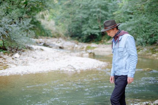 Handsome traveler young man wearing in jeans jacket and hat walking by the river in summer.
