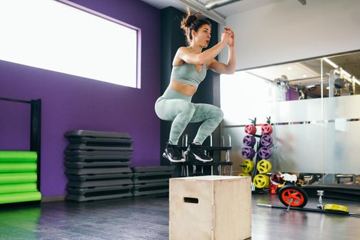 Fitness woman jumping onto a box as part of exercise routine. Caucasian female doing box jump workout at gym.