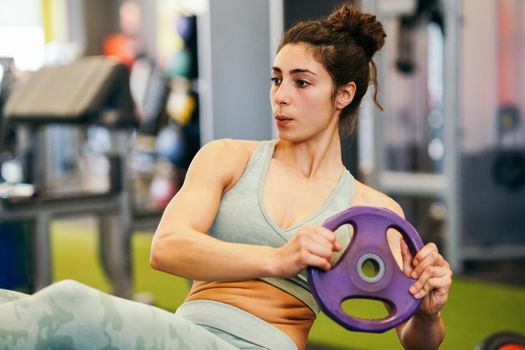 Sporty young female, wearing sportswear, on yoga mat doing situps with plate weights in gym. Fitness woman doing abs crunches.