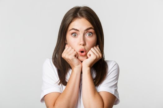 Close-up of intrigued young gossiping girl, leaning on hands and looking wondered at camera, gasping impressed, white background.