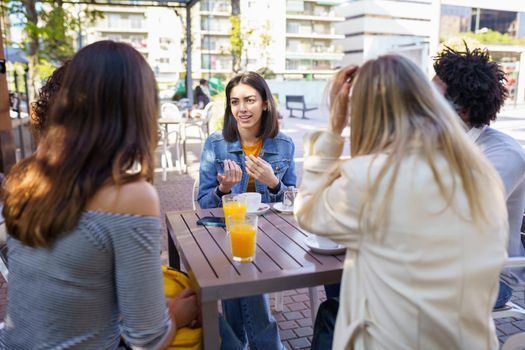 Multi-ethnic group of friends having a drink together in an outdoor bar. Young people having fun.