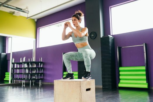 Fitness woman jumping onto a box as part of exercise routine. Caucasian female doing box jump workout at gym.