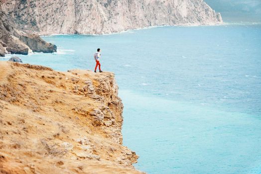 Backpacker traveler young woman standing on edge of cliff over sea.