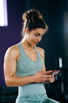 Fitness woman consulting her training on her smartphone sitting in a jump box in the gym