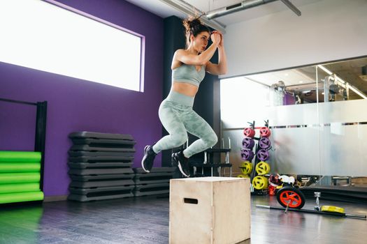 Fitness woman jumping onto a box as part of exercise routine. Caucasian female doing box jump workout at gym.
