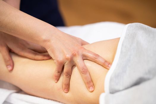 Medical massage at the leg in a physiotherapy center. Female physiotherapist inspecting her patient.