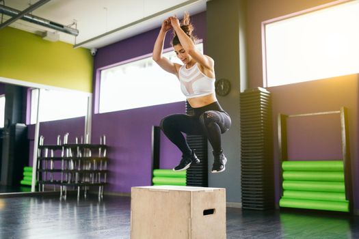 Fitness woman jumping onto a box as part of exercise routine. Caucasian female doing box jump workout at gym.