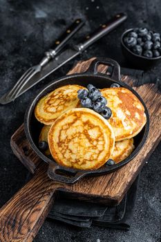 Pancakes with fresh blueberries and maple syrup in a pan. Black background. Top View.