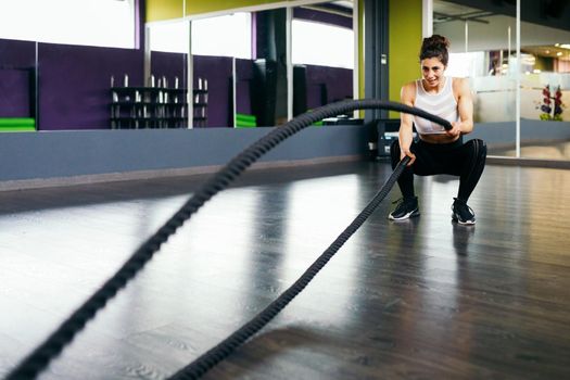 Young and athletic woman using training ropes in a gym. Fitness concept.