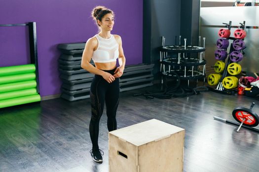 Fitness woman jumping onto a box as part of exercise routine. Caucasian female doing box jump workout at gym.