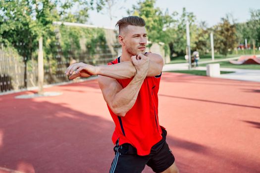 sports man in a red t-shirt on the sports ground doing exercises. High quality photo