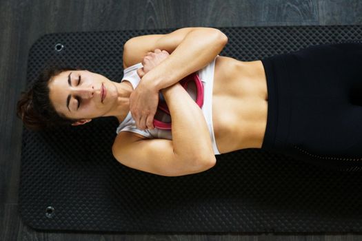 Sporty young female, wearing sportswear, on yoga mat doing situps with plate weights in gym. Fitness woman doing abs crunches.