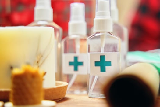 Alcohol antiseptics with the turquoise cross logo on wooden table. Sanitizer, candles and roll of paper. Concept of hand hygiene and prevention from viruses and bacteria.