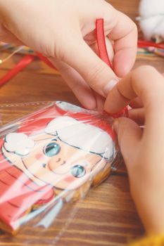 Christmas gifts. Cookies with colored icing on wooden table. Women's hands tie red ribbon on bag of gingerbread in form of pig in Santa Claus hat. New Year's atmosphere.