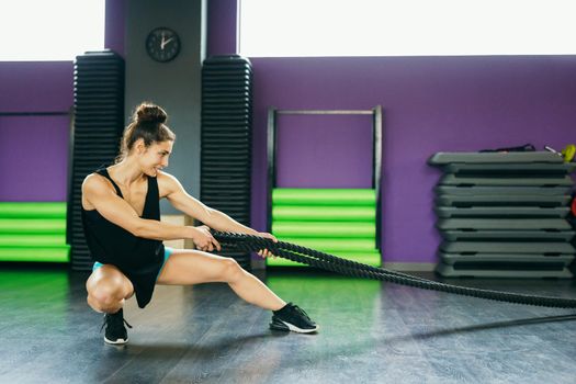 Young and athletic woman using training ropes in a gym. Fitness concept.