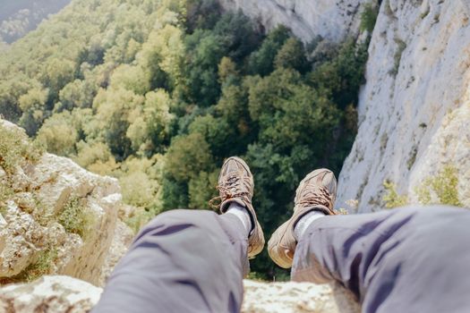 Explorer young man sitting on edge of cliff over valley, point of view.