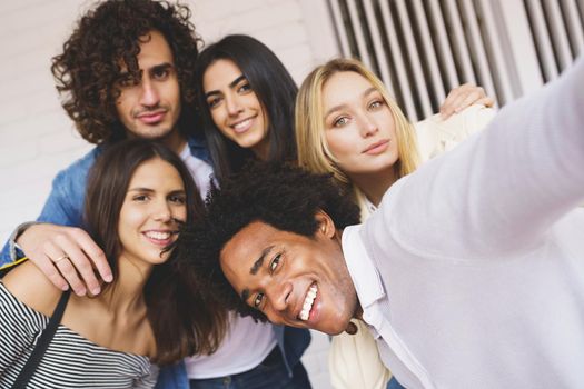 Multi-ethnic group of friends taking a selfie together while having fun in the street. Black man with afro hair in the foreground.