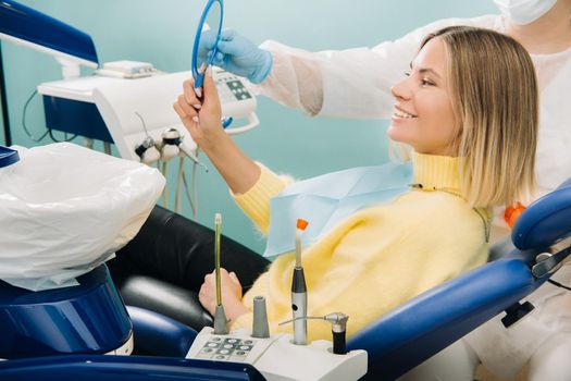 The girl smiles and looks in the mirror in dentistry.