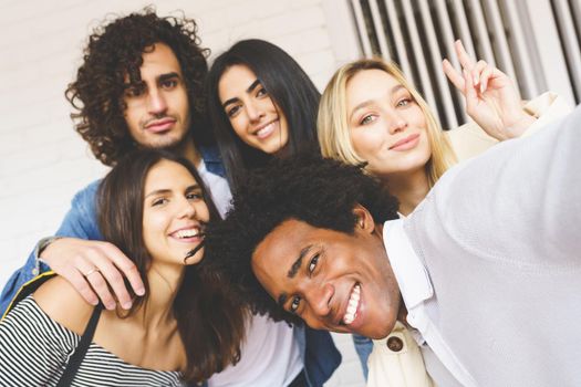 Multi-ethnic group of friends taking a selfie together while having fun in the street. Black man with afro hair in the foreground.