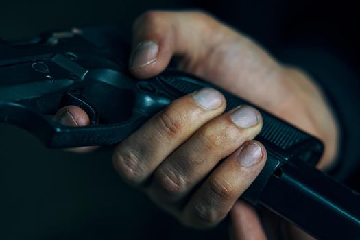 Man inserts drum of cartridges into pistol. Reloading gun close-up. Firearms in hand on dark background. Defense or attack.