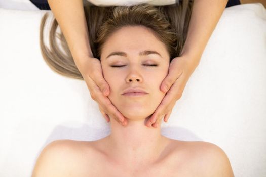 Young woman receiving a head massage in a spa center. Female patient is receiving treatment by professional therapist.