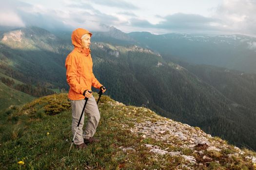 Explorer traveler young woman with trekking poles standing on background of mountains.