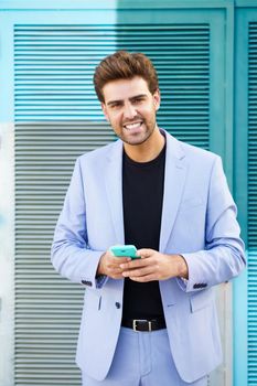 Young businessman wearing blue suit using a smartphone in urban background. Man with formal clothes in the street.