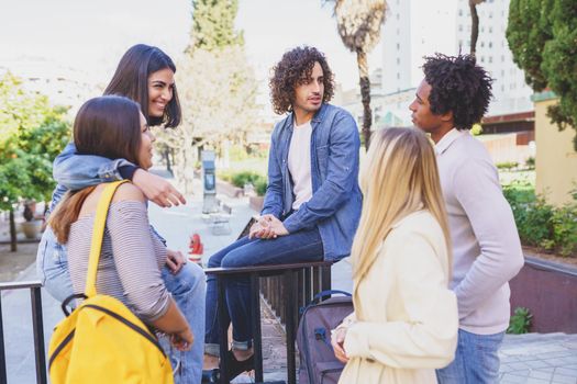 Multi-ethnic group of friends gathered in the street leaning on a railing. Young people having fun together.