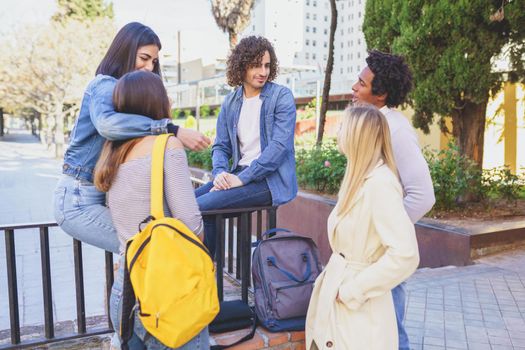 Multiracial group of young people talking together in the street. Students socializing.